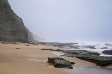 Praia do Magoito, Sintra, Portekiz - Mart 2023: Okyanus manzarası, kayalar, kum ve dalgalar sahilde. Atlantik Okyanusu
