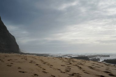 Praia do Magoito, Sintra, Portekiz - Mart 2023: Okyanus manzarası, kayalar, kum ve dalgalar sahilde. Atlantik Okyanusu