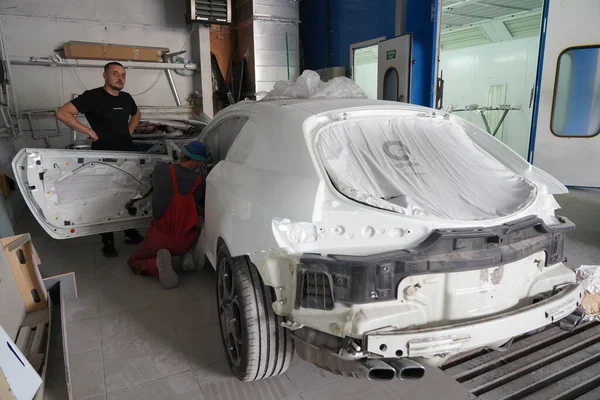Kyiv, Ukraine - August 12, 2023: Paint shop at the car service station. Paint shop master. Painting a car in a paint booth. Disassembled car after painting.