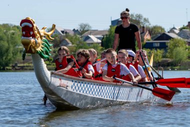 Ukrayna, Bila Tserkva, Kyiv Bölgesi - 01 Mayıs 2024: Şehrin orta kesimindeki gölde çocuklar kürek çekiyor. Kano sporu bölümü. Ejderha teknesi, ejderha kafası ve kuyruğu olan bir kano..