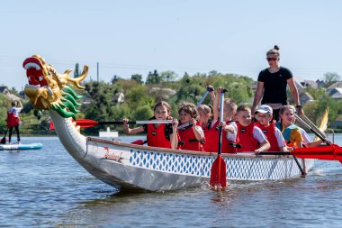 Ukrayna, Bila Tserkva, Kyiv Bölgesi - 01 Mayıs 2024: Şehrin orta kesimindeki gölde çocuklar kürek çekiyor. Kano sporu bölümü. Ejderha teknesi, ejderha kafası ve kuyruğu olan bir kano..