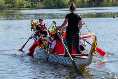 Ukrayna, Bila Tserkva, Kyiv Bölgesi - 01 Mayıs 2024: Şehrin orta kesimindeki gölde çocuklar kürek çekiyor. Kano sporu bölümü. Ejderha teknesi, ejderha kafası ve kuyruğu olan bir kano..