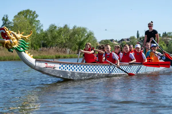 Ukrayna, Bila Tserkva, Kyiv Bölgesi - 01 Mayıs 2024: Şehrin orta kesimindeki gölde çocuklar kürek çekiyor. Kano sporu bölümü. Ejderha teknesi, ejderha kafası ve kuyruğu olan bir kano..