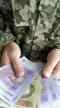 Askeri üniformalı erkek eller parayı tutar. Ukrayna Hrivnia 'sı bir askerin elinde. Ukrayna piksel askeri üniformasının arka planına karşı para.