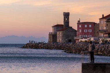 Piran, Slovenya - 3 Kasım 2024: İkamet evleri olan şehir sokağı. Gün batımında evleri olan deniz kıyısında. Piranski svetilnik