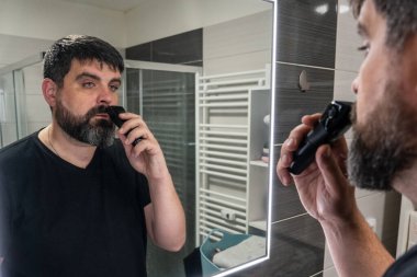 Adam banyoda sakalını kesiyor. Sakal bakımı, elektrikli jilet. Banyo aynasında sakallı bir adamın yansıması..