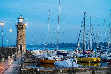 Desenzano del Garda, İtalya - 6 Kasım 2024: Yatlı deniz feneri ve marina manzarası. Garda Gölü, rıhtım ve dağ manzarası.