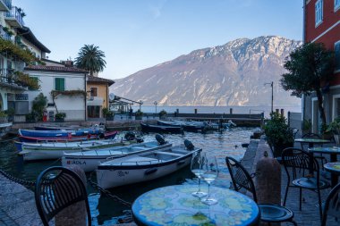 Limone Sul Garda, İtalya - 7 Kasım 2024: Garda Gölü ve dağların manzarası. Şarap kadehleri, arka planda kayıklar ve dağlar..
