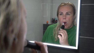 Banyoda dişlerini elektrikli diş fırçasıyla fırçalayan sarışın kadın..