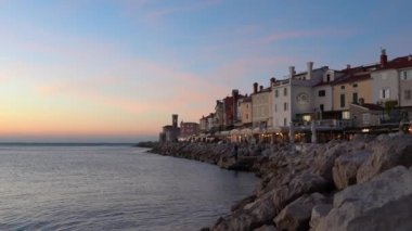 Piran, Slovenya - 3 Kasım 2024: İkamet evleri olan şehir sokağı. Gün batımında evleri olan deniz kıyısında. Piranski svetilnik