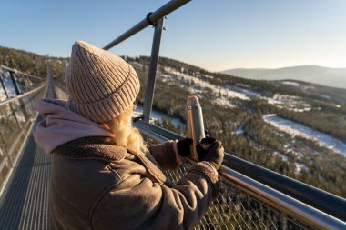 Sky Bridge 721, Aşağı Moravya, Çek Cumhuriyeti - 1 Aralık 2024: Bir kadın kış dağ manzarasına bakarken termostan sıcak çay içiyor. Dağ beldesi Dolni Morava