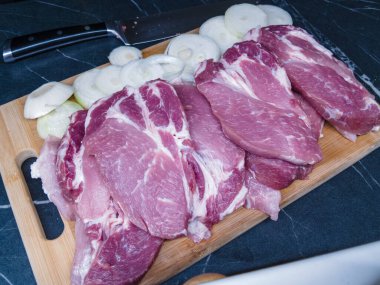 Dilimlenmiş soğan ve keskin bir mutfak bıçağıyla ahşap bir kesme tahtasına yerleştirilmiş taze çiğ domuz bifteği. Yemek pişirme, yemek hazırlama ya da yemek tarifleri için ideal.