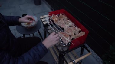 Sıcak bir açık verandada kırmızı bir mangal mangalı kurulur. Yakınlarda gerekli ızgara araçları ve gaz lambası, çakmak gazı, briketler gibi kullanıma hazır eşyalar bulunuyor..