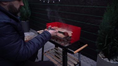 Sıcak bir açık verandada kırmızı bir mangal mangalı kurulur. Yakınlarda gerekli ızgara araçları ve gaz lambası, çakmak gazı, briketler gibi kullanıma hazır eşyalar bulunuyor..