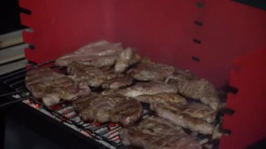 Sıcak bir açık verandada kırmızı bir mangal mangalı kurulur. Yakınlarda gerekli ızgara araçları ve gaz lambası, çakmak gazı, briketler gibi kullanıma hazır eşyalar bulunuyor..