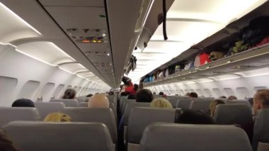 Viyana, Avusturya - 18 Ocak 2025: Uçağın içinde yolcu alımı. El bagajı başlık kutusuna konur. Bir uçuş görevlisi uçağa binerken yolcuya yardım eder..