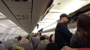 Viyana, Avusturya - 18 Ocak 2025: Uçağın içinde yolcu alımı. El bagajı başlık kutusuna konur. Bir uçuş görevlisi uçağa binerken yolcuya yardım eder..