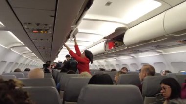 Viyana, Avusturya - 18 Ocak 2025: Uçağın içinde yolcu alımı. El bagajı başlık kutusuna konur. Bir uçuş görevlisi uçağa binerken yolcuya yardım eder..