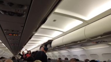 Viyana, Avusturya - 18 Ocak 2025: Uçağın içinde yolcu alımı. El bagajı başlık kutusuna konur. Bir uçuş görevlisi uçağa binerken yolcuya yardım eder..