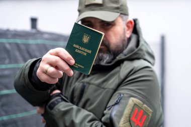 A man in a military uniform holds a military registration document (military ID, military card). Mobilization for war. Mobilization of men into the Ukrainian army. A pocket of a military uniform and a chevron of a branch of the Ukrainian armed forces clipart