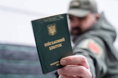 A man in a military uniform holds a military registration document (military ID, military card). Mobilization for war. Mobilization of men into the Ukrainian army. A pocket of a military uniform and a chevron of a branch of the Ukrainian armed forces clipart