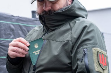 A man in a military uniform holds a military registration document (military ID, military card). Mobilization for war. Mobilization of men into the Ukrainian army. A pocket of a military uniform and a chevron of a branch of the Ukrainian armed forces clipart