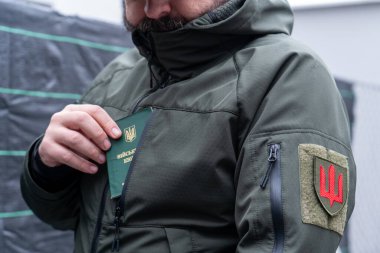 A man in a military uniform holds a military registration document (military ID, military card). Mobilization for war. Mobilization of men into the Ukrainian army. A pocket of a military uniform and a chevron of a branch of the Ukrainian armed forces clipart