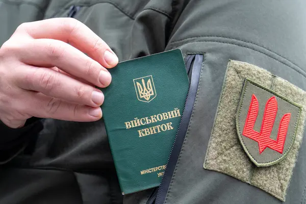 Askeri üniformalı bir adamın elinde askeri ruhsat belgesi (askeri kimlik, askeri kimlik) vardır. Savaş için seferberlik. Adamların Ukrayna ordusuna girmesi. Bir askeri üniforma cebi ve Ukrayna silahlı kuvvetlerinin bir kolu.