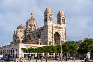 Marsilya, Fransa, 2 Şubat 2025: Çağdaş binaların çerçevelediği modern bir şehir caddesinden alınan La Major Katedrali (Marsilya Katedrali) manzarası. Katedral 'in görkemli mimarisi modern çevresiyle çelişiyor ve onun işaretini gösteriyor.