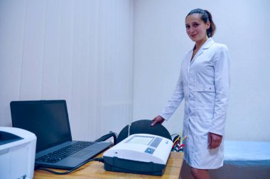 Kyiv, Ukrayna - 23 Aralık 2021: Beyaz önlüklü bir tıp uzmanı teşhis işlemi için elektrokardiyograf (ECG) hazırlıyor. Doktor, kalp faaliyetlerini izlemek için kullanılan mavi plastik ampullü birden fazla vakum kabı elektrotları tutuyor.
