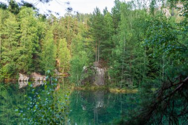 Adrspach, Çek Cumhuriyeti - 20.07.2025: Piskovna Gölü 'ndeki Adrspach-Teplice Kayaları manzarası. Ağaçların ve kayaların arasında bir orman gölü.
