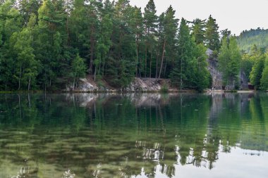 Adrspach, Çek Cumhuriyeti - 20.07.2025: Piskovna Gölü 'ndeki Adrspach-Teplice Kayaları manzarası. Ağaçların ve kayaların arasında bir orman gölü.