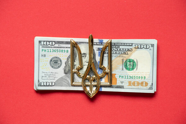 The coat of arms of Ukraine lies on one hundred dollars on a red background, the economy of Ukraine, business and finance