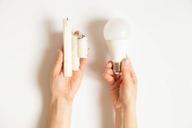 LED ampul ve mumlar beyaz arka plandaki bir kızın ellerinde, elektrik ve tasarruf seçimi, ışık yok