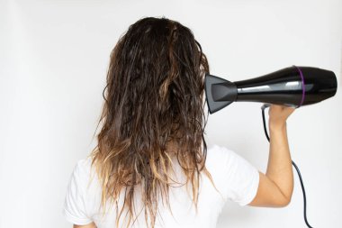 Kız saçını beyaz bir arka planda saç kurutma makinesiyle, saç kurutma makinesiyle ve kuaförle kurutuyor.
