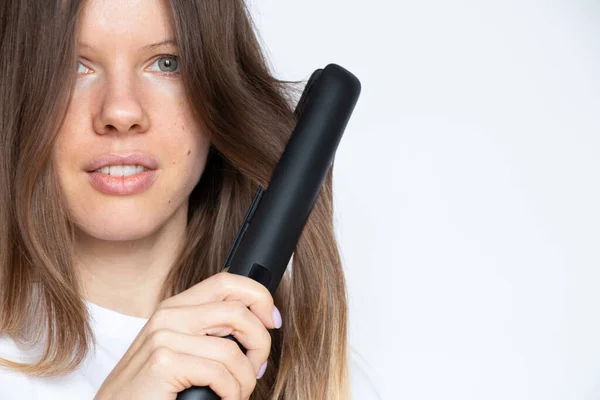 The girl straightens her hair with straightening tongs on a white background, hair care, curlers and a hairdresser