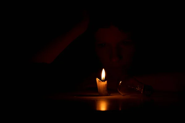 暗闇の中の女の子はろうそくと電球で家の暗闇の中のテーブルに座って 家で光のない人々 — ストック写真