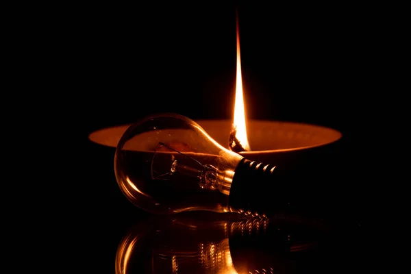 A rope in oil lies on a plate and burns, and next to it lies a light bulb on the mirror in the dark, a homemade candle on the mirror, there is no light