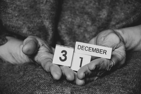 December 31 is written on the cubes that an old woman holds in her hands, black and white photo, holiday