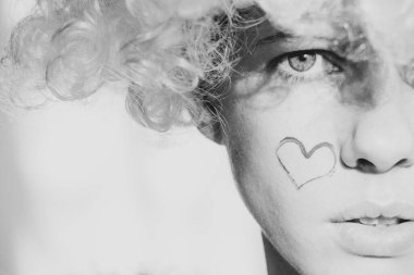 Kanatlı, kıvırcık saçlı, yanağında boyalı bir kalple melek gibi giyinmiş bir kız izole bir arka planda, bir melek ve aşk.