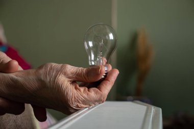 An incandescent lamp in the hands of an old woman vozli batteries in the apartment, people without light, power outages