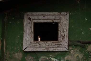 Three candles stand on a broken window of an old residential building, view from the street through the window, the light of a candle in a window in Ukraine, people without light at home