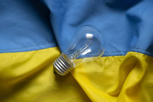 An incandescent lamp lies on the flags of Ukraine, people without light in Ukraine due to Russian missile attacks, war, crisis