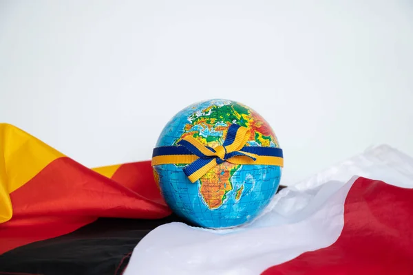Globe tied with a ribbon with the flag of Ukraine lies on the flags of Germany and Poland on a white background close-up