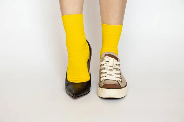 Different shoes on the girl\'s legs, high heeled shoes and sports sneakers in yellow socks on a white background, fashion