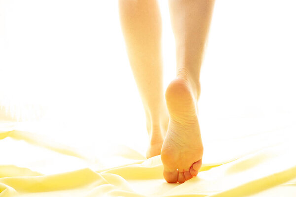 Women's feet on a yellow fabric in the sunlight, girl's foot