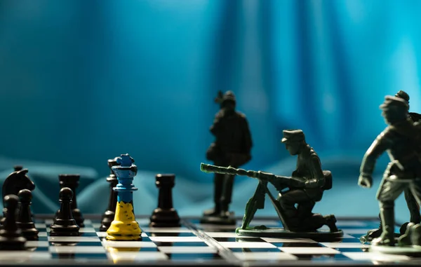 Chess king in the colors of the flag of Ukraine on a chessboard with chess and next to several plastic soldiers, war 2023