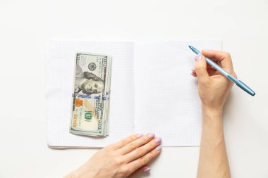 Kadın eli bir deftere yazar ve dolar beyaz arka planda, iş dünyasında yatar.