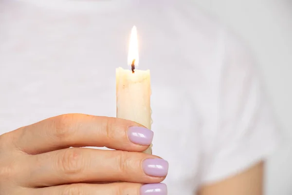 A burning candle in the hands of a girl on a white background in the light of day, culture