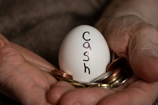 An egg with the inscription cash and coins in the hands of a grandmother, money